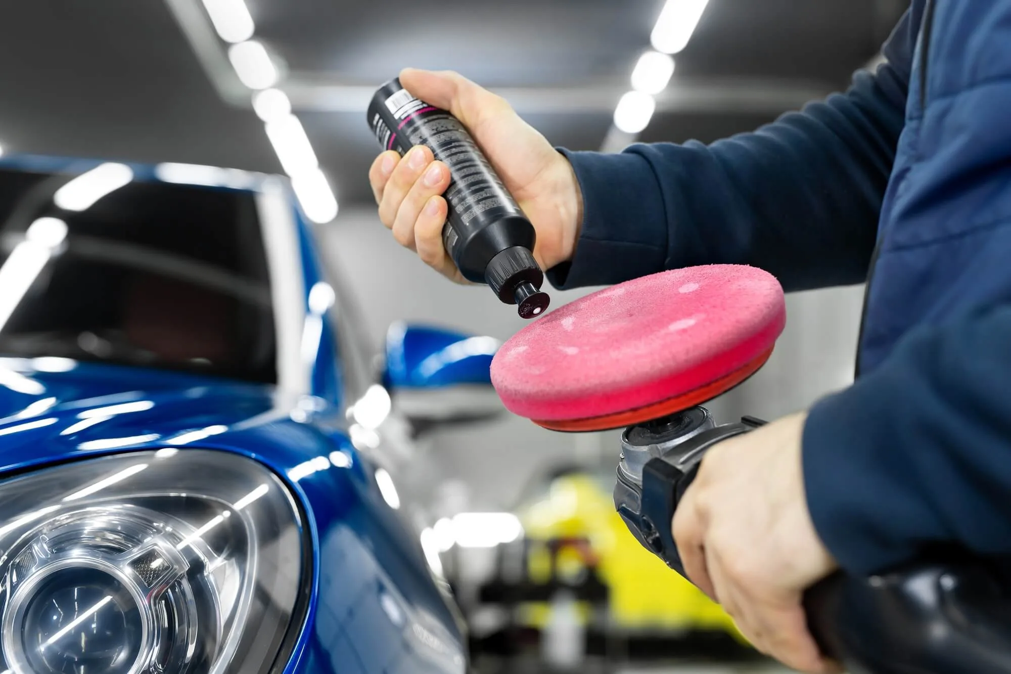 Detailing a car in studio, the master applies paste or wax to the car body polishing machine.